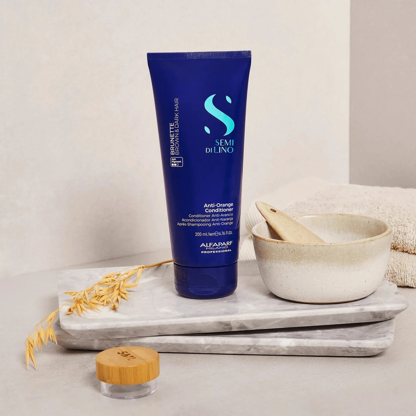 Blue tube of anti-orange conditioner for brown and dark hair on marble tray with bowl and towel
