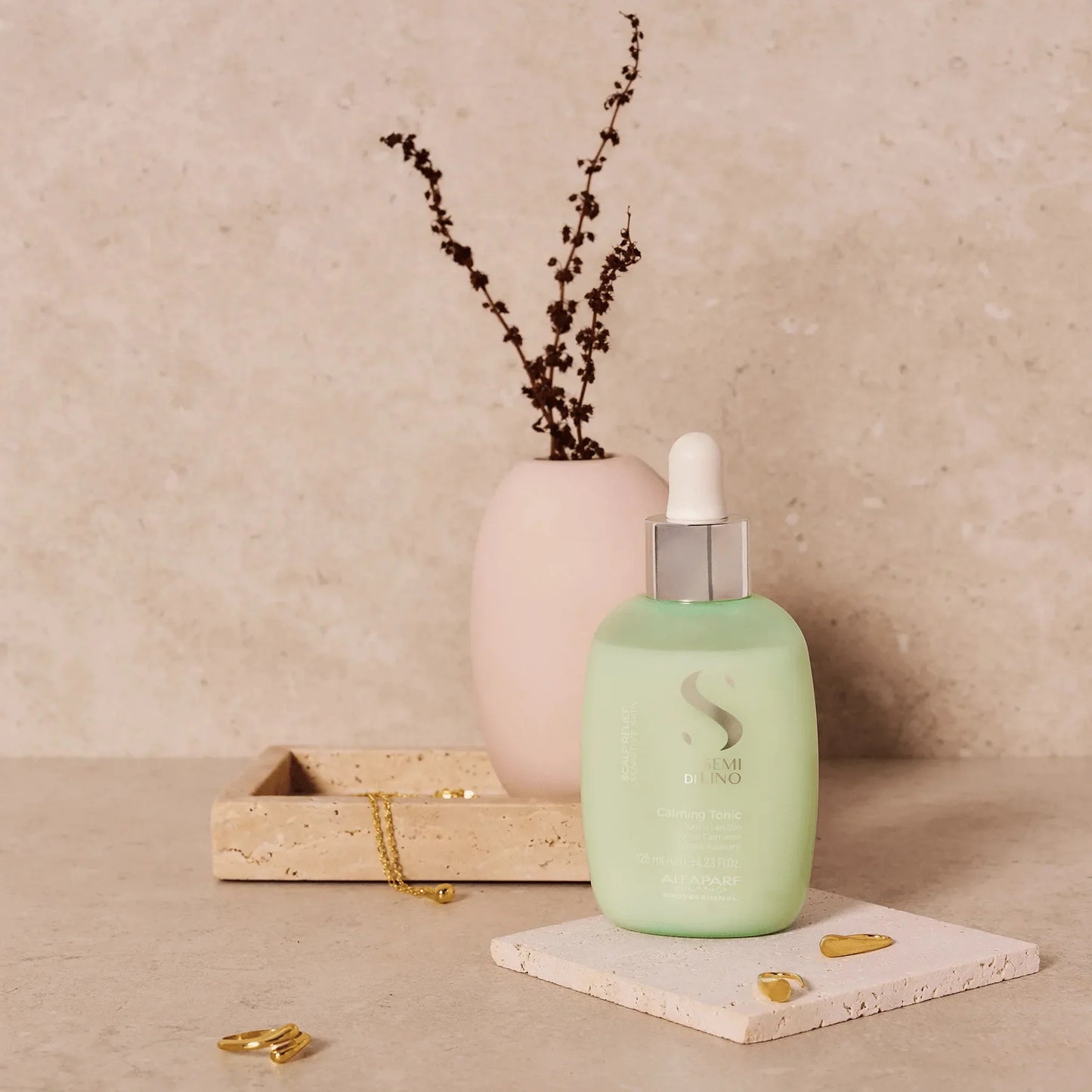Green scalp relief calming tonic bottle with dropper, staged on a stone background with jewelry.