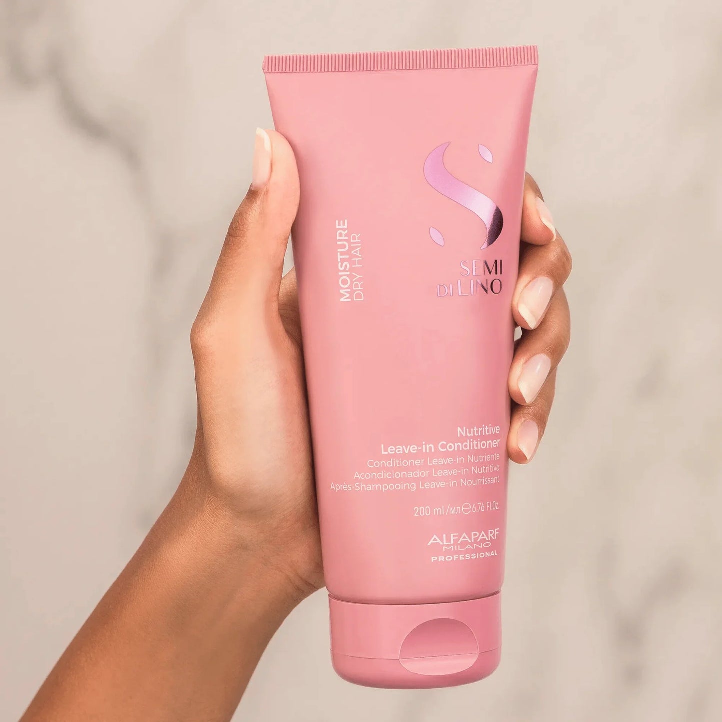 Hand holding pink bottle of Alfaparf Semi Di Lino Moisture Nutritive Leave-in Conditioner