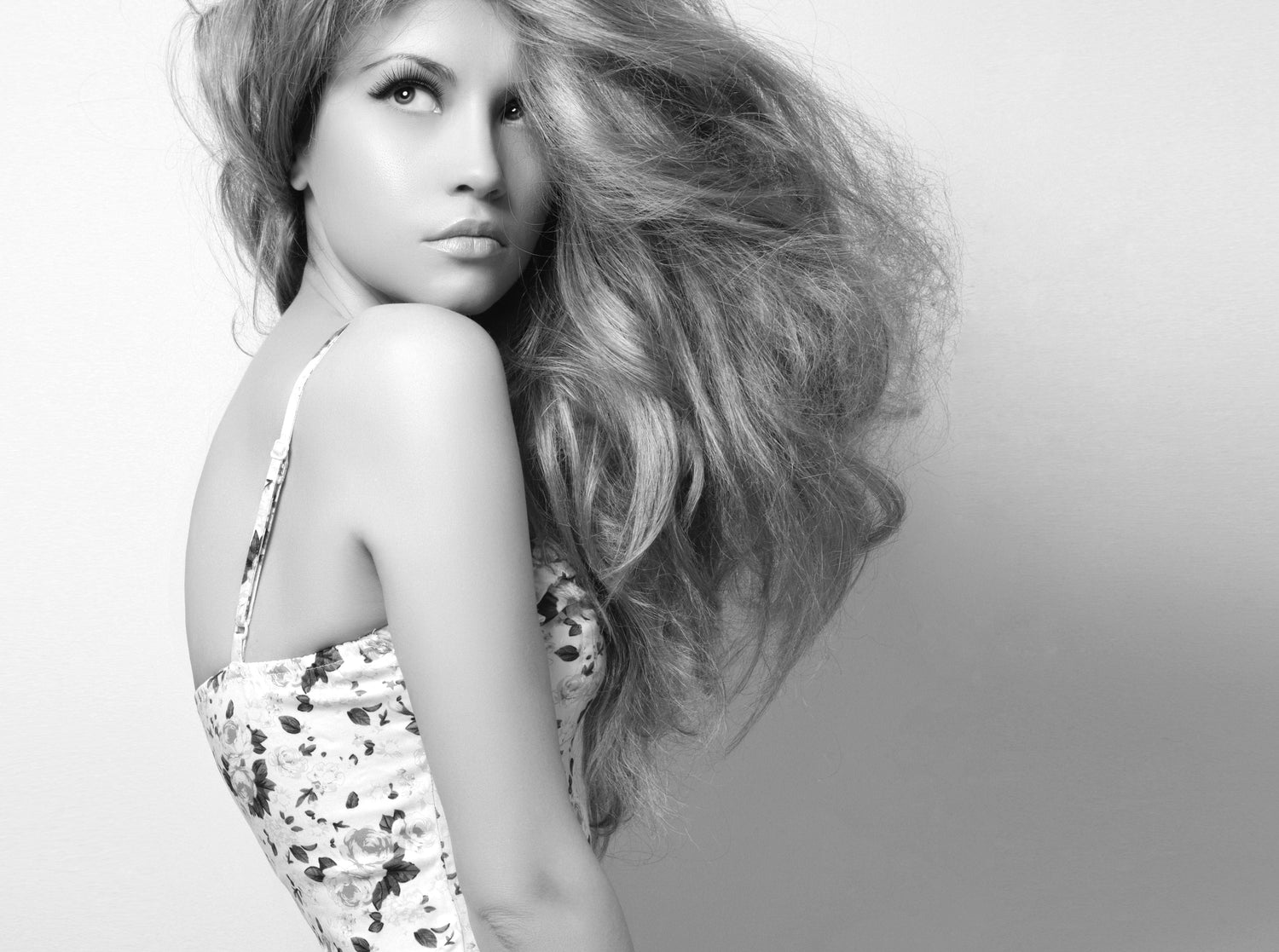 Woman with flowing hair and a floral dress on a plain background